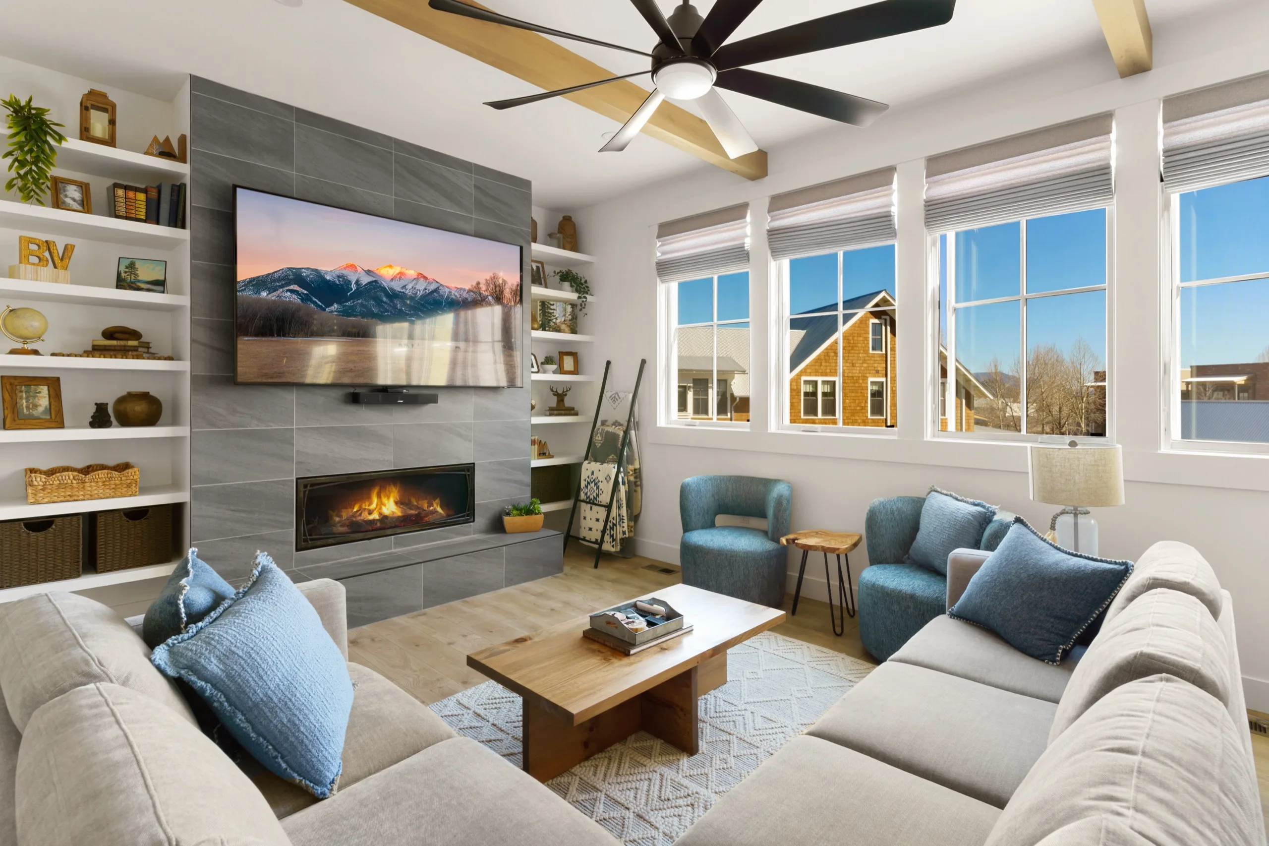 Living room with a grey sectional facing a tiled gas fireplace, built-in shelves either side and blue accents throughout