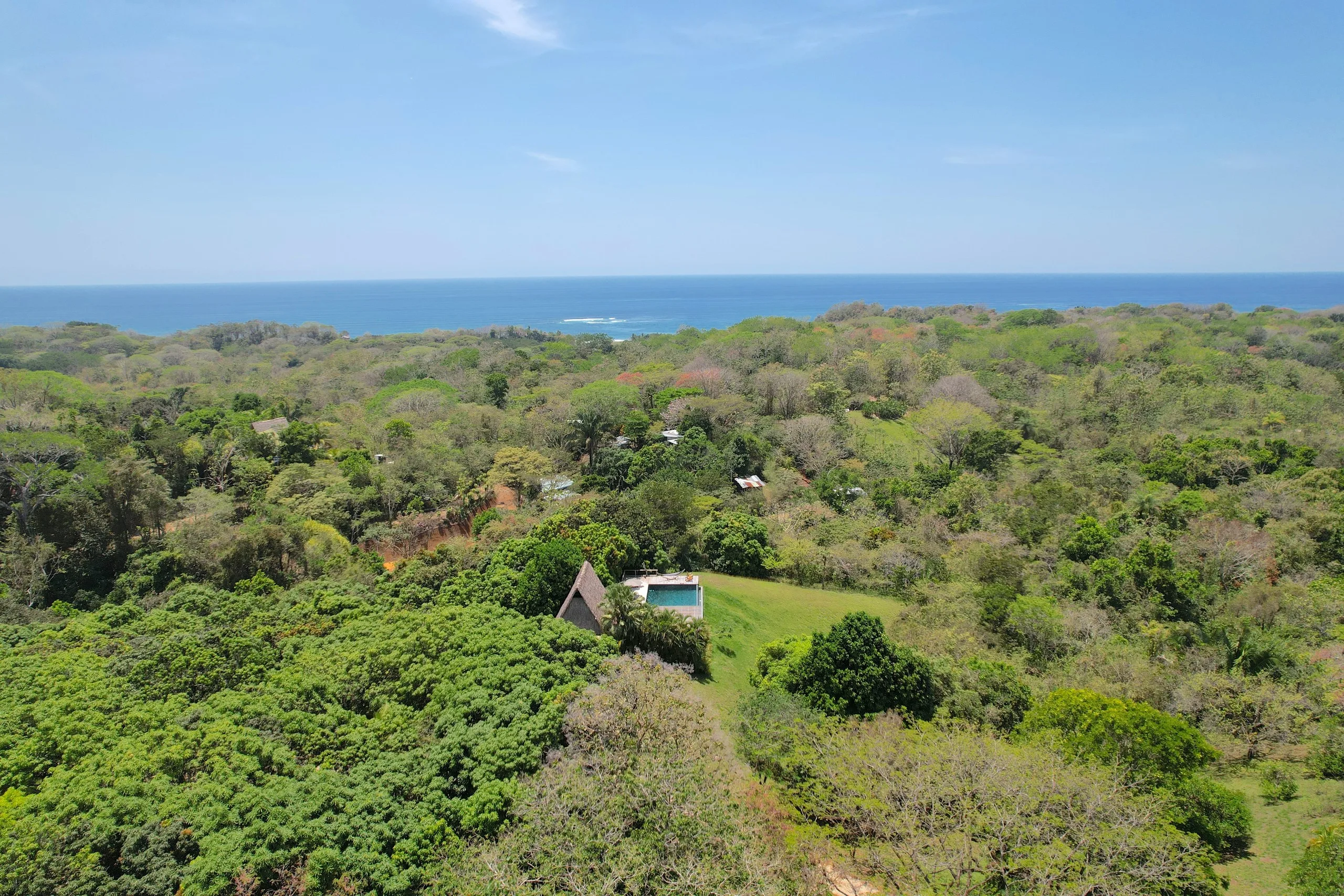 From the air: a single house and its pool in a clearing, jungle running unbroken to the Pacific