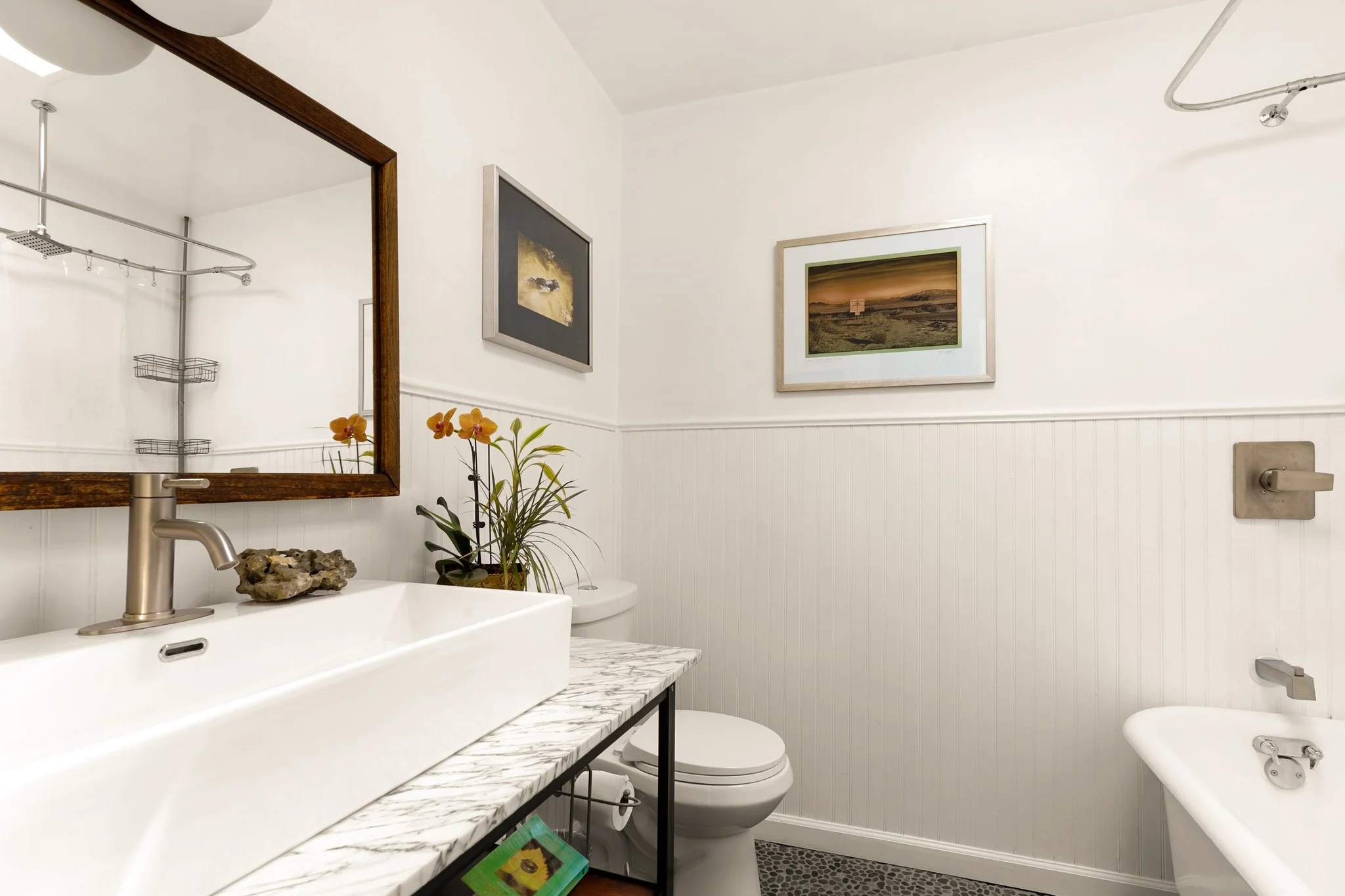Bathroom in white beadboard with a marble-topped vanity, vessel basin and a clawfoot tub beneath framed desert prints