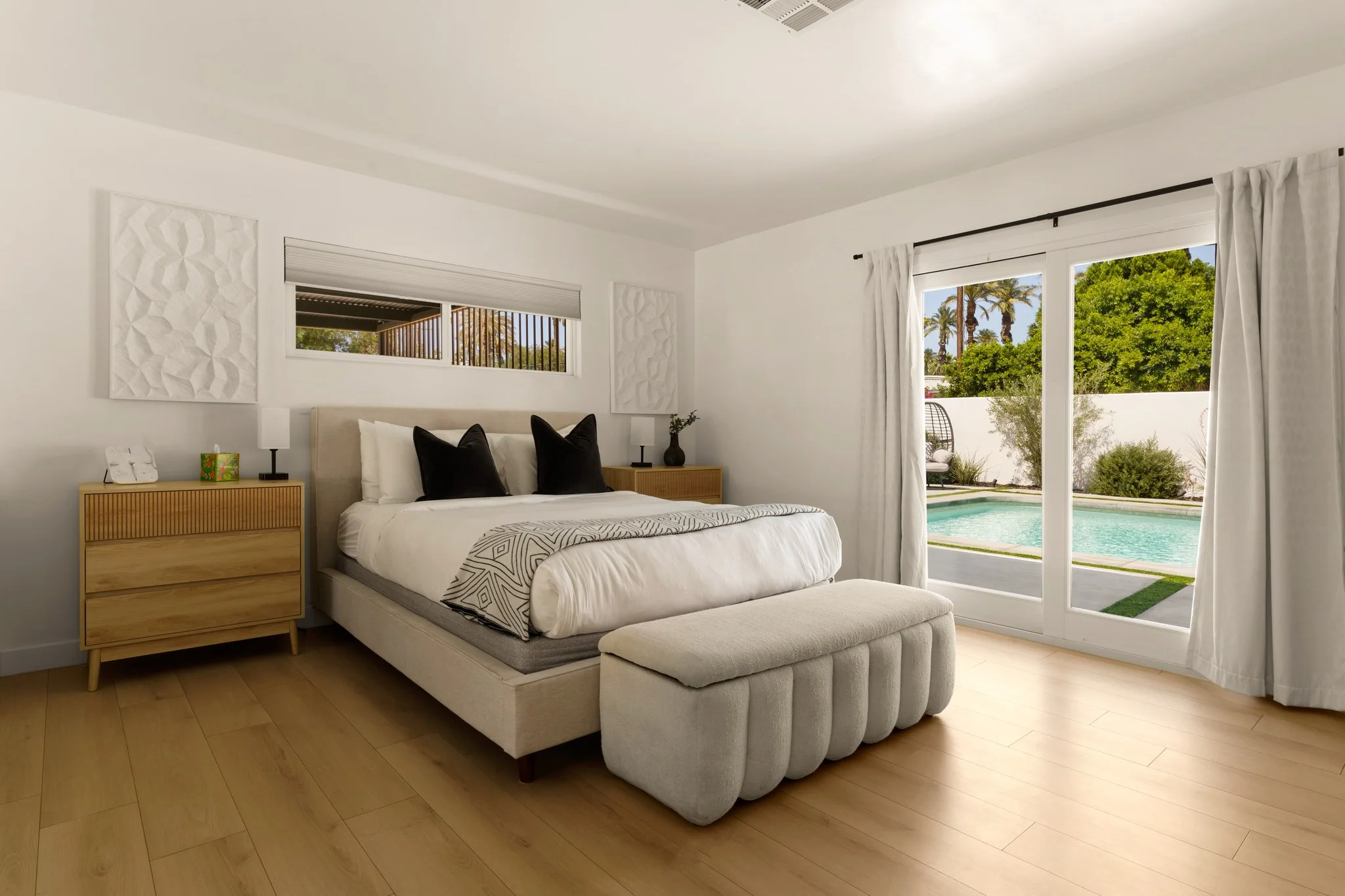 Bedroom in white and pale oak, upholstered bench at the foot of the bed and doors open to the pool