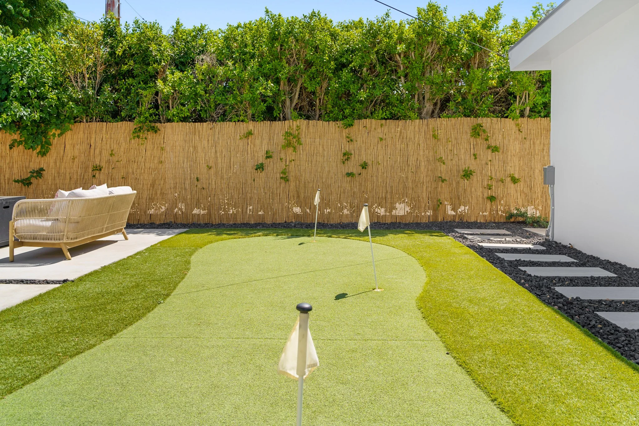 Putting green behind a reed fence and a wall of hedge, a cabana chair in the far corner