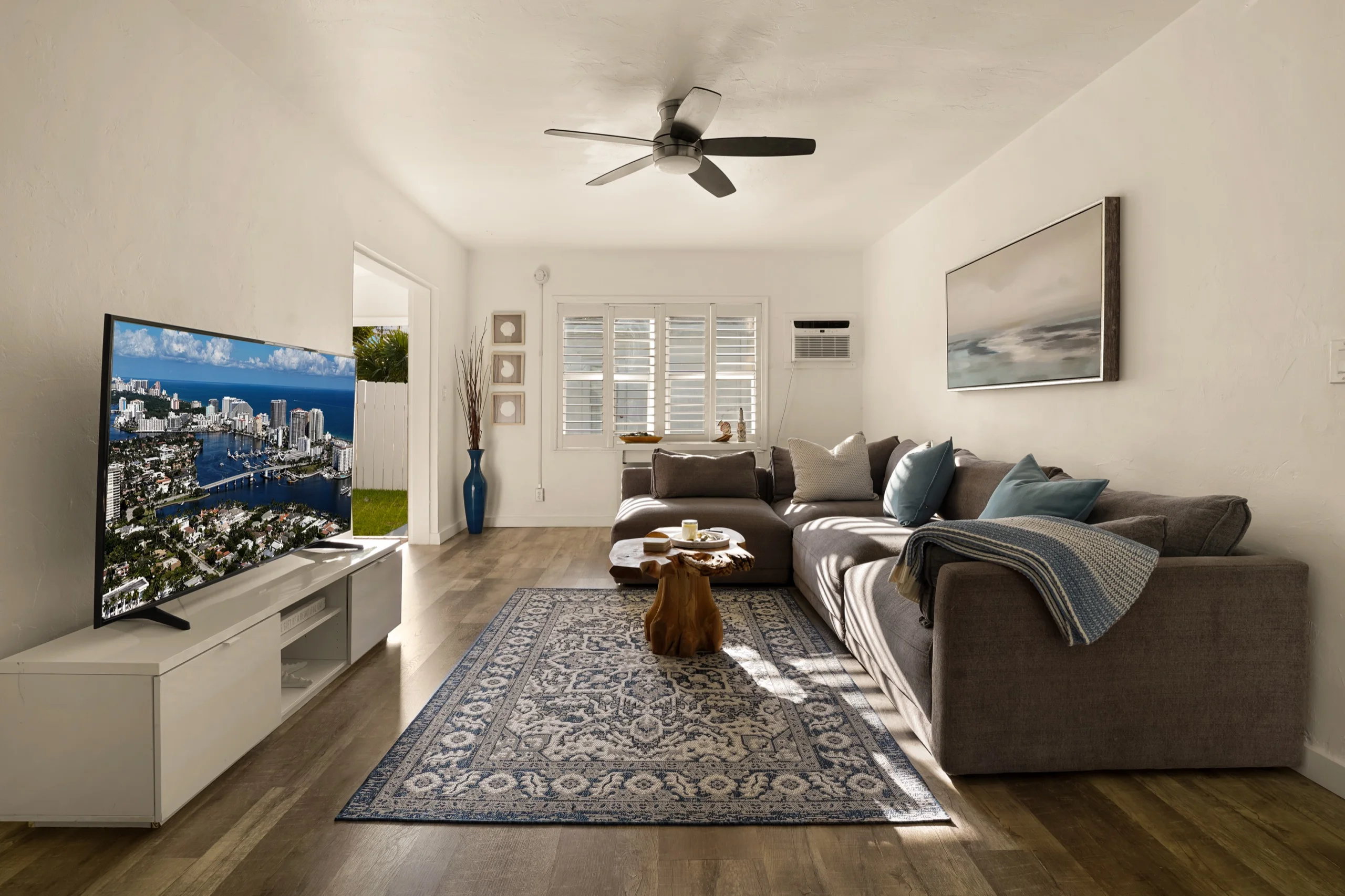 Den with a grey sectional, patterned rug and afternoon light through plantation shutters