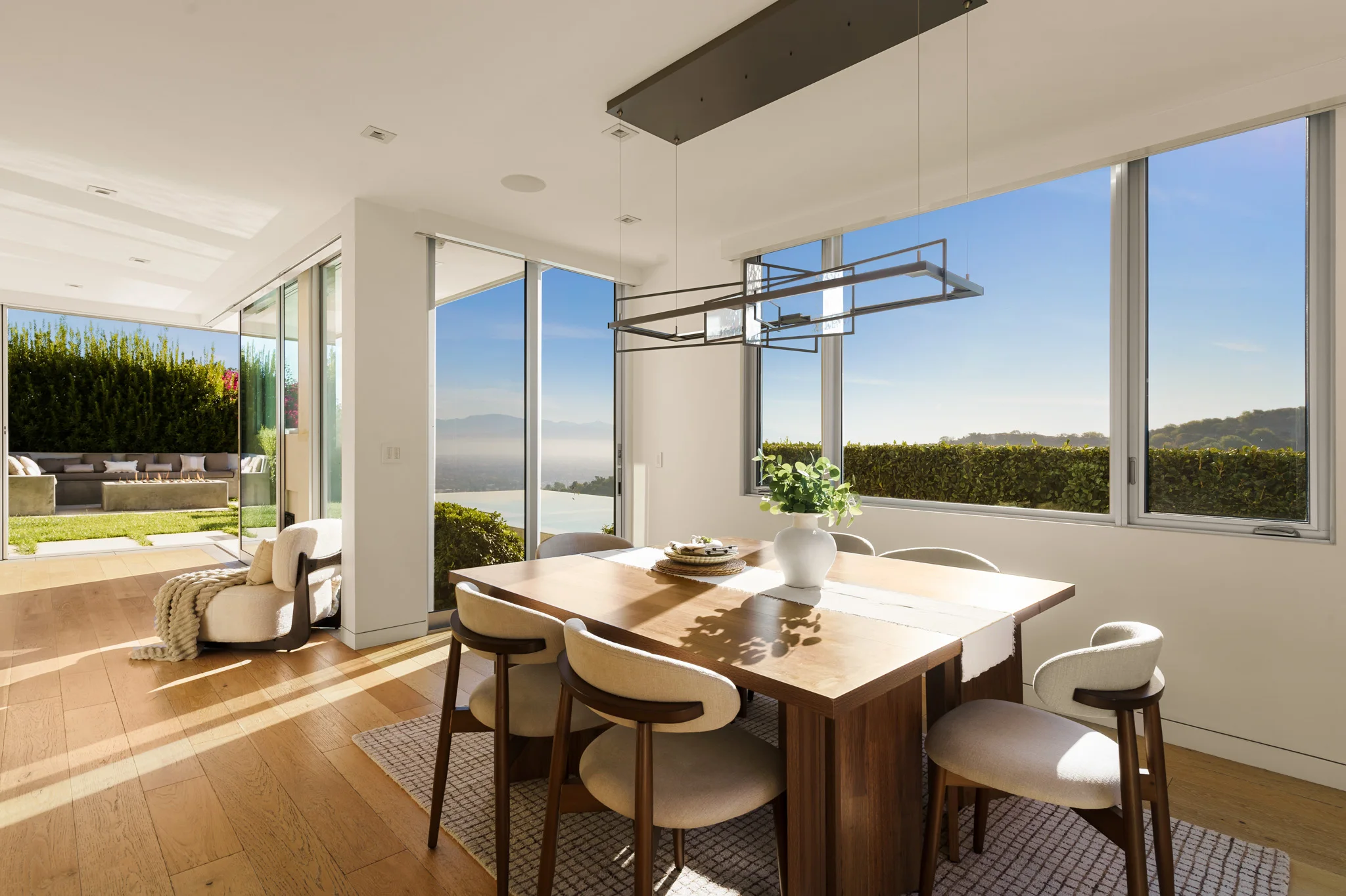 Dining table set for six in a corner of glass, the living room and the terrace visible past it