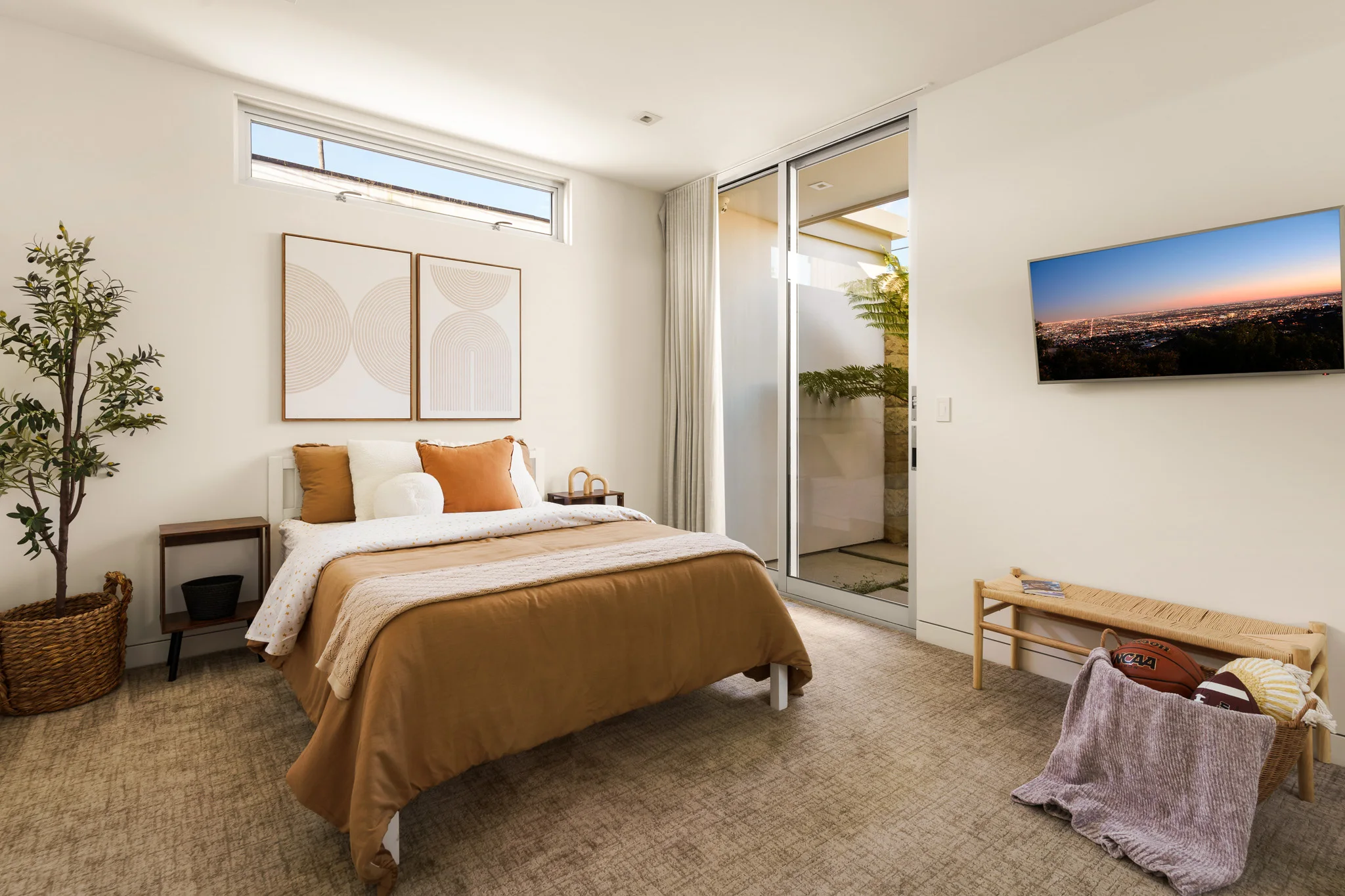 Bedroom with a caramel throw and a pair of prints above the bed, clerestory light and an olive tree in the corner
