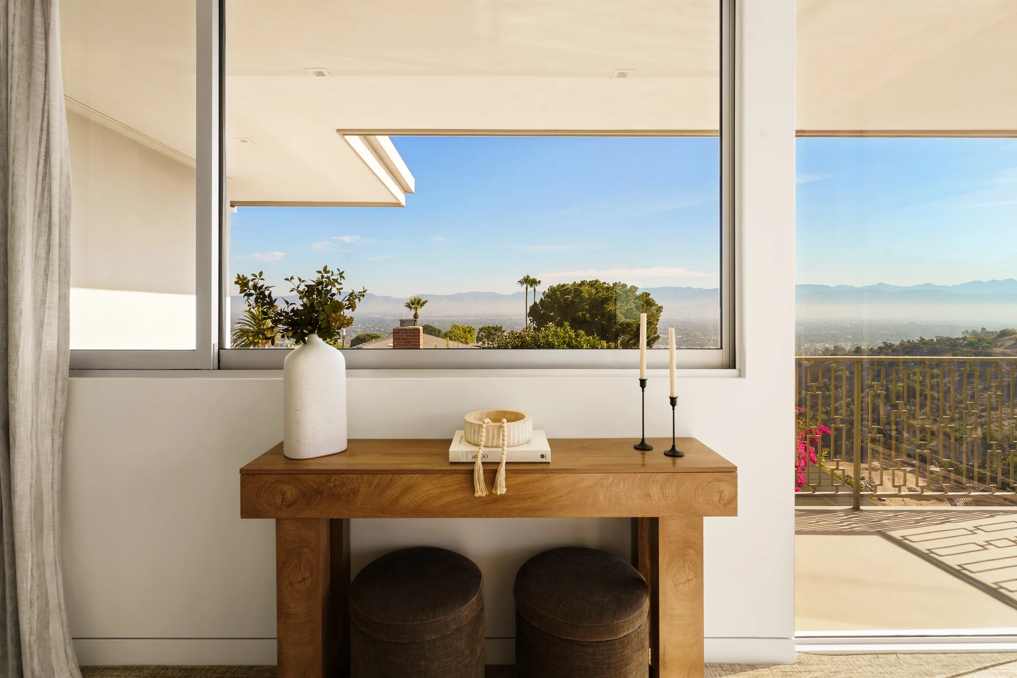 Oak console against a picture window, ceramic vase and taper candles framed against distant hills