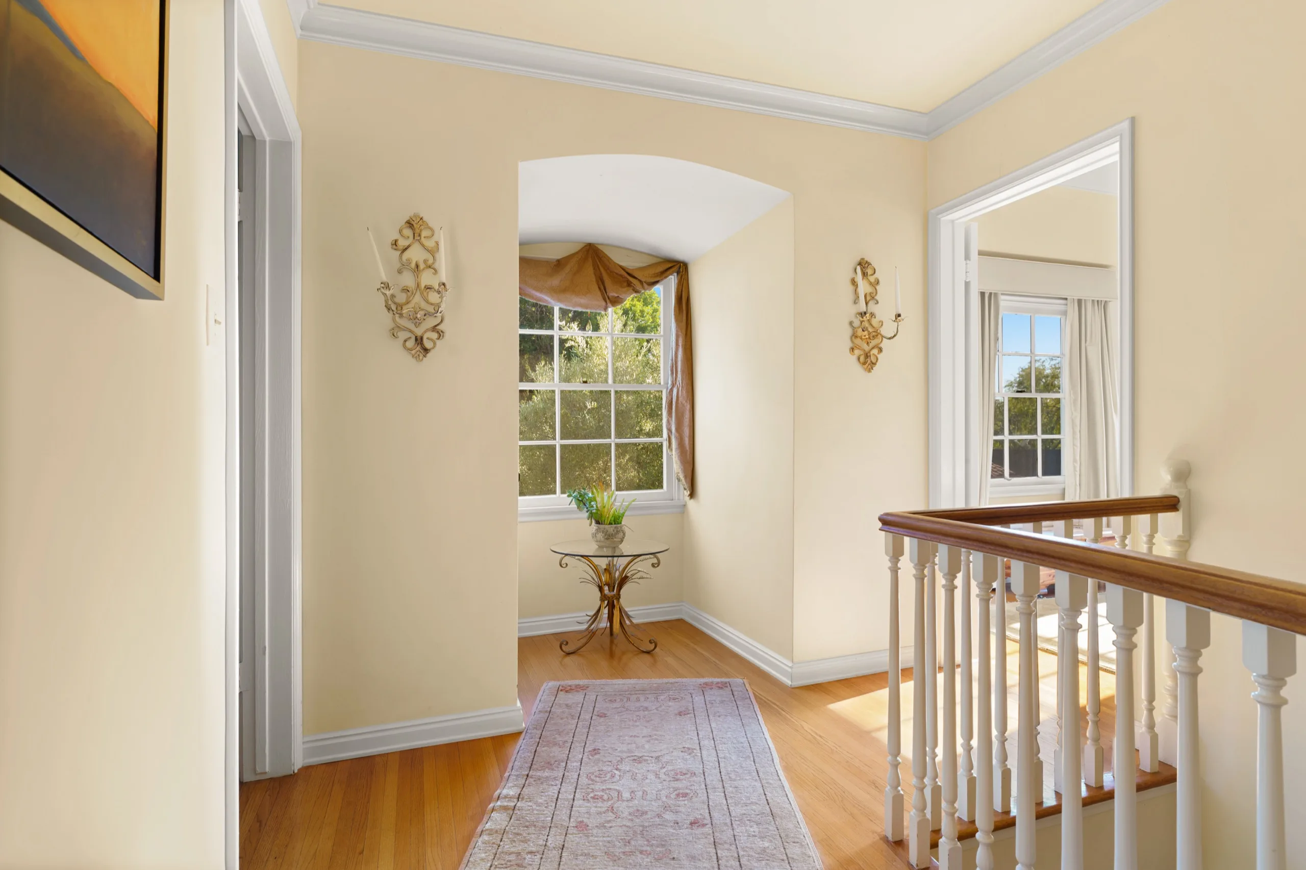 Upstairs landing with an arched alcove, brass sconces and a turned banister above the stair