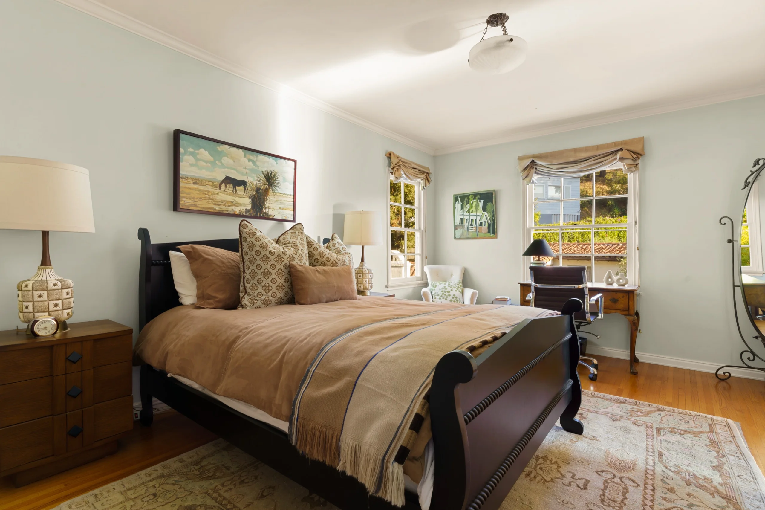 Bedroom in pale green with a dark sleigh bed, a writing desk set into the bay window