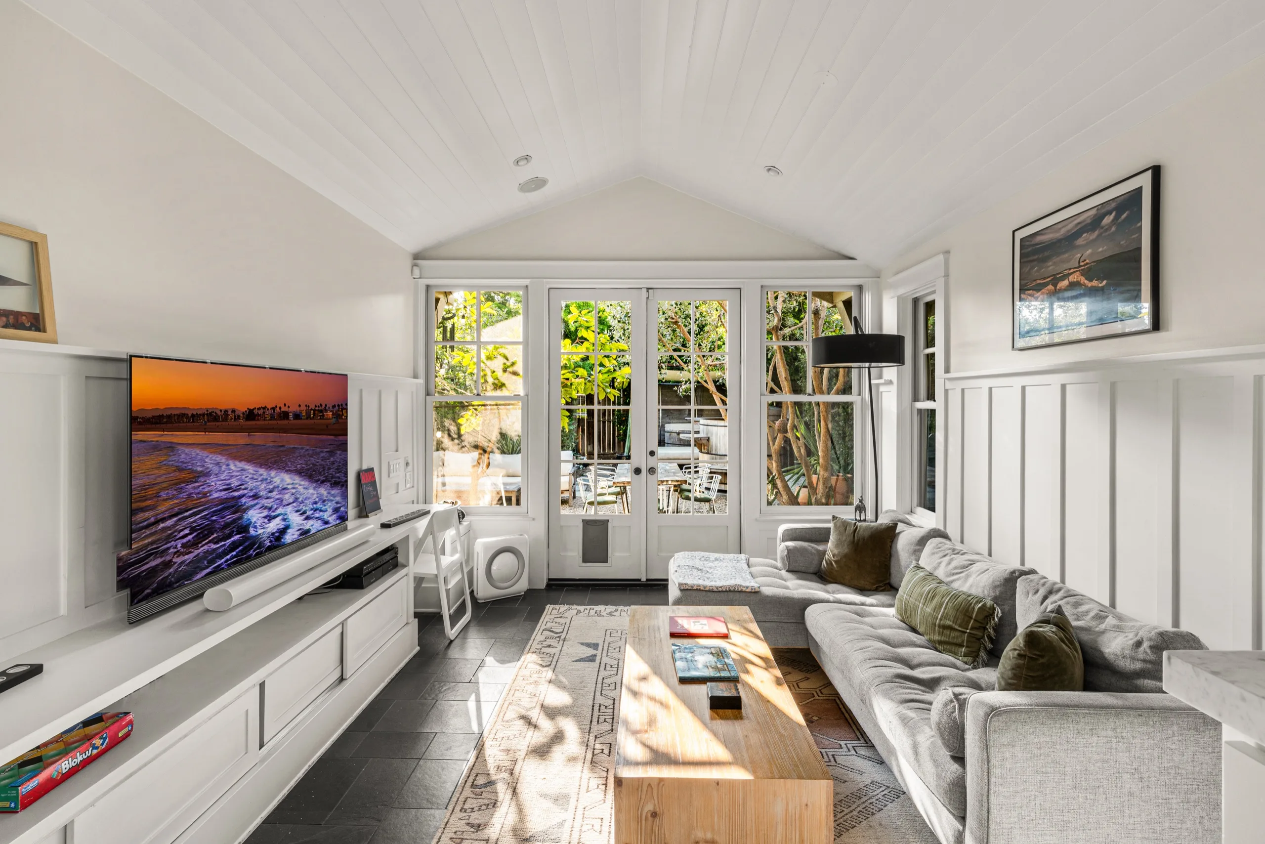 Vaulted living room in white board-and-batten, French doors open to a planted courtyard