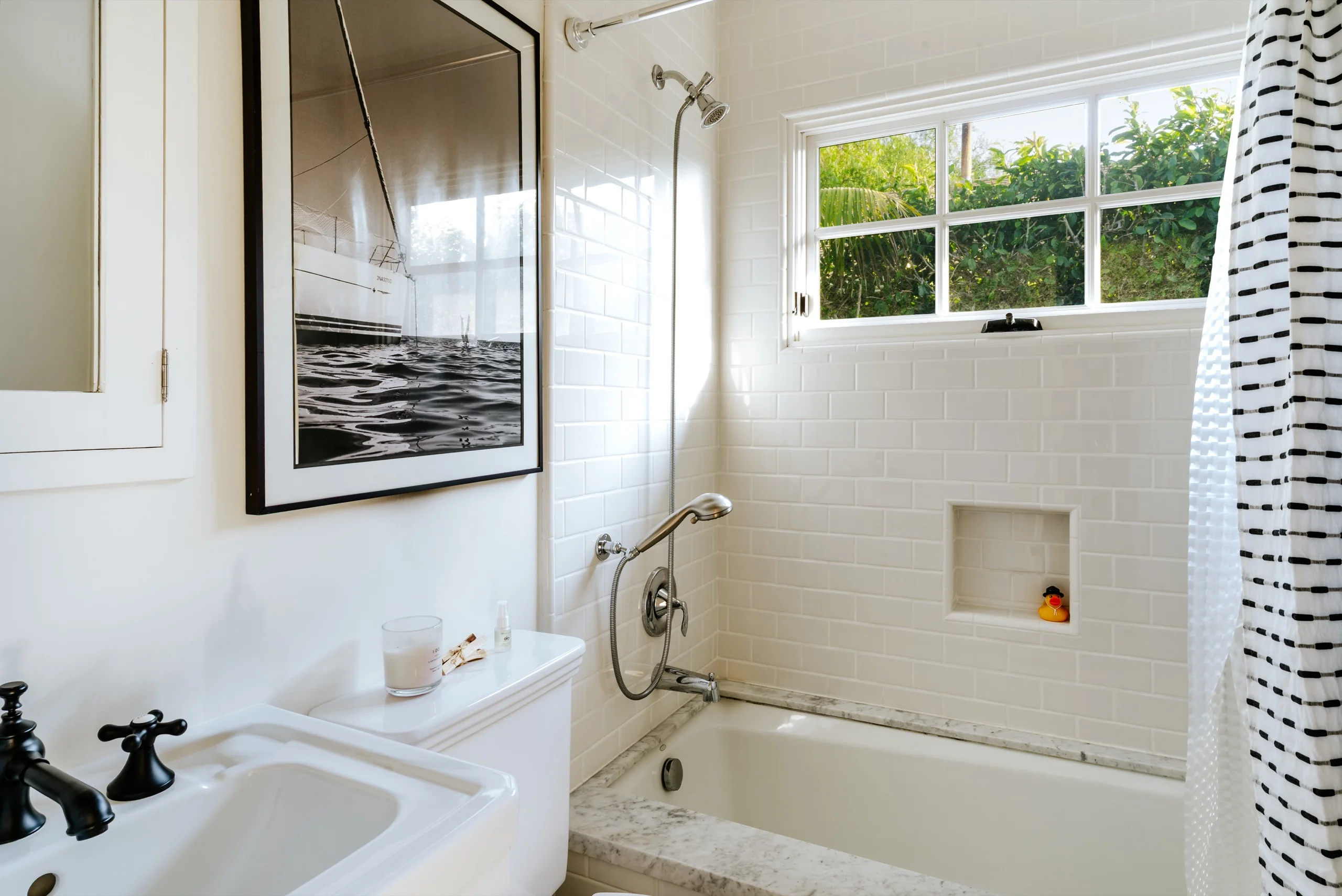 Subway-tiled bathroom with a cast-iron tub, a framed seascape and a striped shower curtain