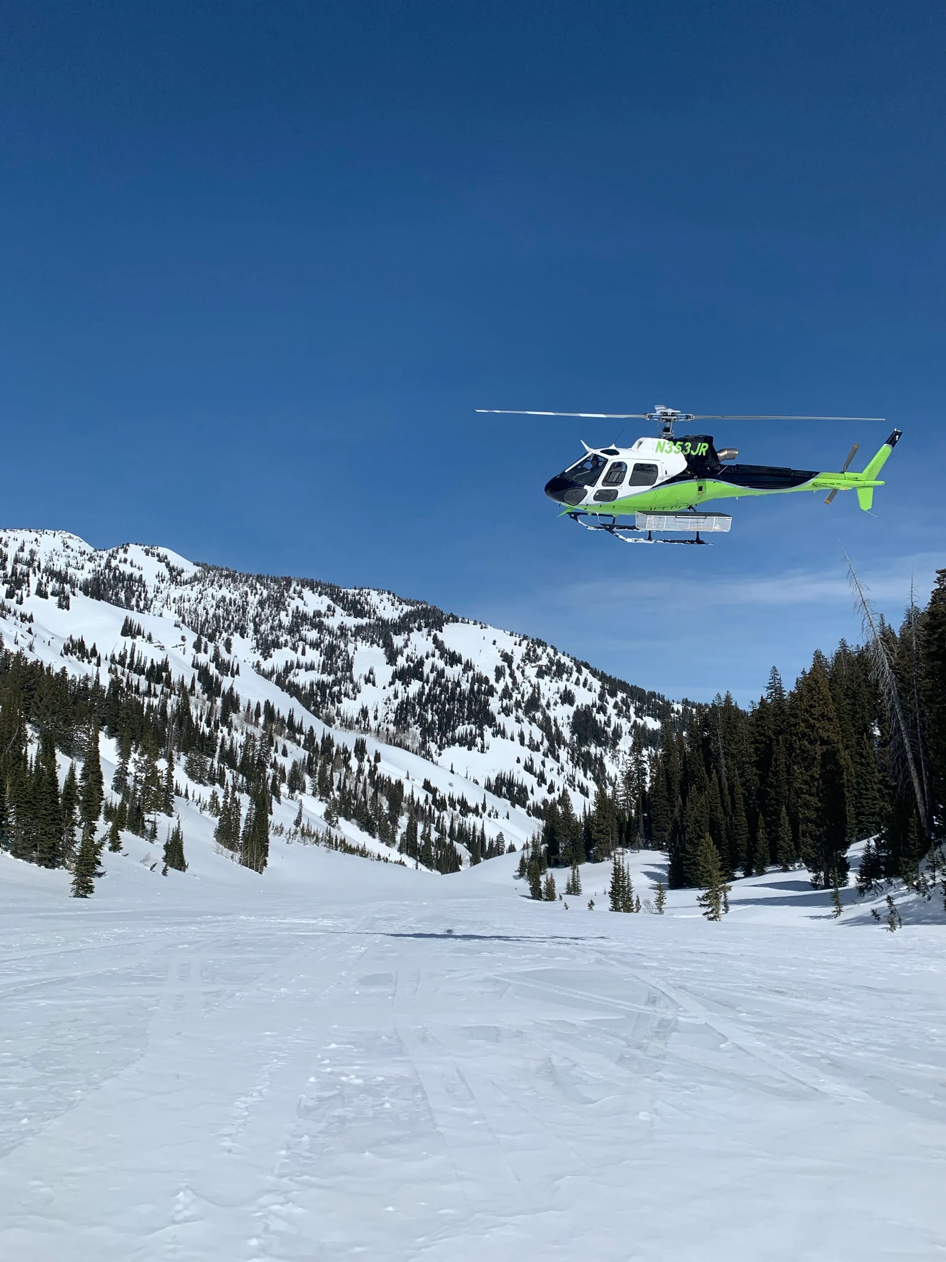 Helicopter lifting off from packed snow below a steep alpine ridge