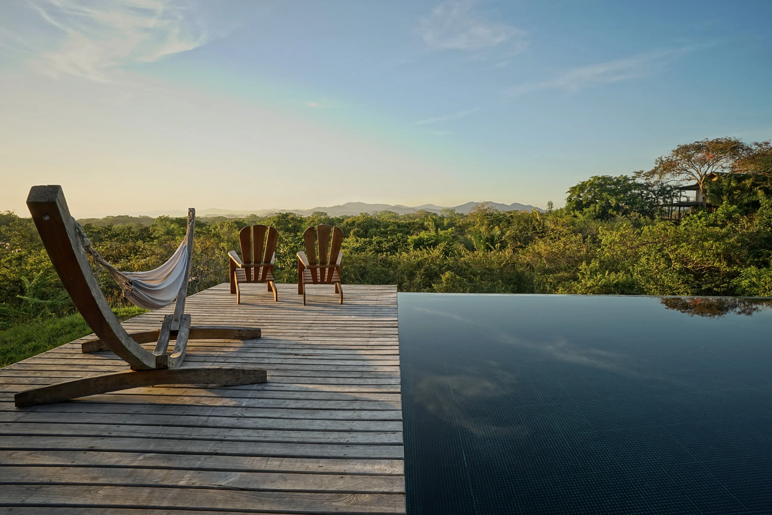 Timber deck above the canopy at first light, a hammock and two chairs facing the ridges