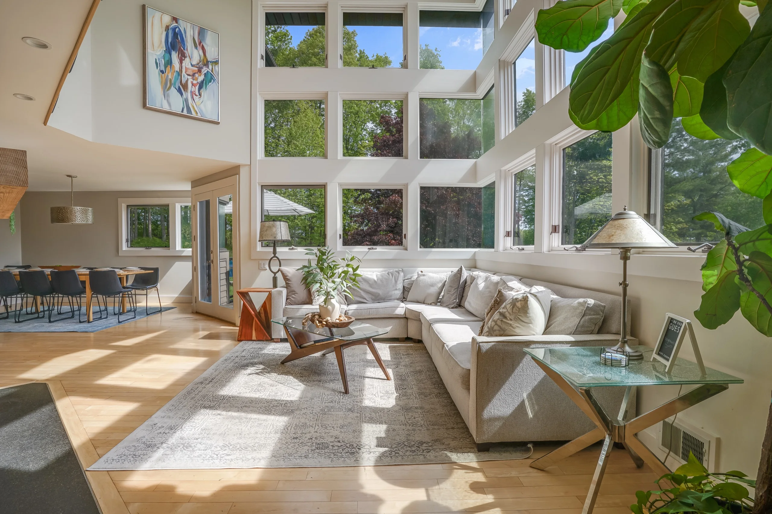 Double-height living room with a pale sectional beneath a two-storey window wall, dining table beyond