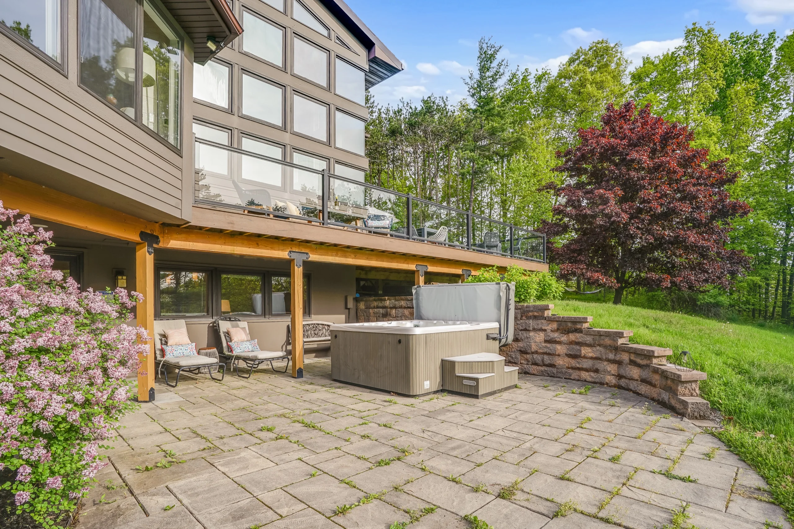 Flagstone patio below the house with a hot tub against a stone retaining wall, lilac in flower